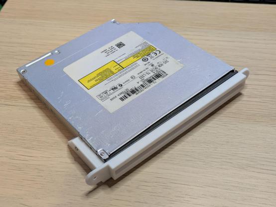 A photo of a slim CD drive from a computer, with a thin 3D printed faceplate bolted onto it.