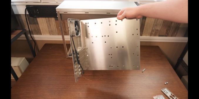 Clint from LGR holdong the toolfree-removeable mainboard tray of a aluminium PC case up to show that all the mainboard components can be installed on it without hassle.