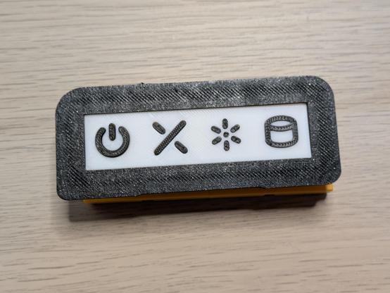 A photo of a 3D printed part with power, reset, light and cylinder symbols. The reset symbol on this one is a broken or interrupted X shape.
