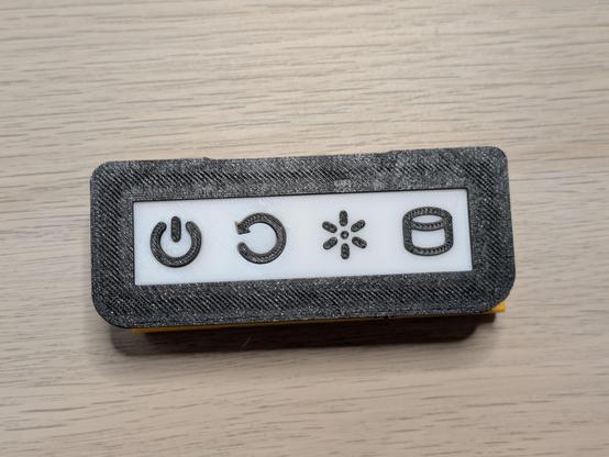 A photo of a 3D printed part with power, reset, light and cylinder symbols. The reset symbol on this one is a circle with an arrow pointing around its circumference.