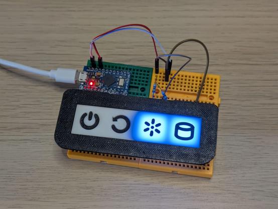 The same arrangement from the first photo except a 3D printed frame and cover has been placed over the buttons and LEDs. They form part of the front panel for a PC, with power and reset buttons, and power and drive lights. The two lights are brightly lit with diffuse blue light showing in a square through the white cover.