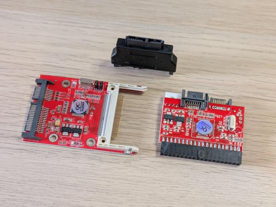 A photo of some internal computer parts. There's an adapter to plug a CompactFlash memory card into a serial ATA controller, nother to plug a slim CD drive into the same, and then a third to attach both SATA drives to a parallel ATA controller.