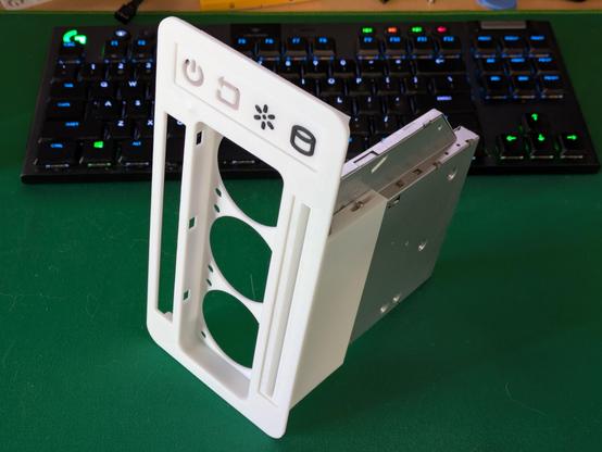 A photo of a partially assembled 3D printed computer case sitting on a desk. So far it's just the front of the case with a few things screwed on - a slim CD drive is on one side with a slot poking through the front panel, a large rectangular gap with spaces for 3 cooling fans, an empty slot opposite the CD drive which will be filled with keyboard and joystick ports, and a panel across the top with power and reset buttons, and power and drive activity lights. It's sitting on a green mousepad in front of a keyboard for scale - the front panel measure about ten by 20 centimetres.