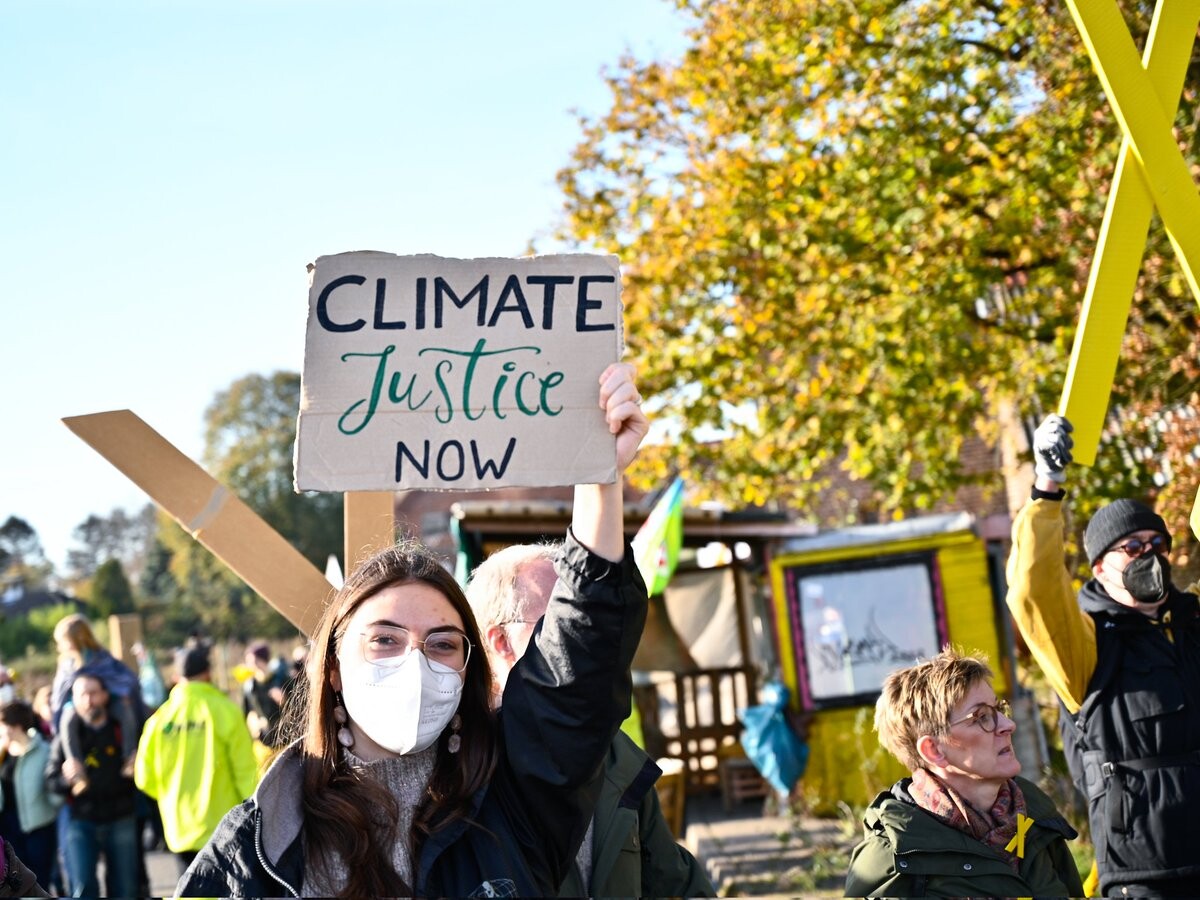 Demo mit gelben X-Zeichen aus Holz. Eine Person mit Demoschild: Climate Justice now