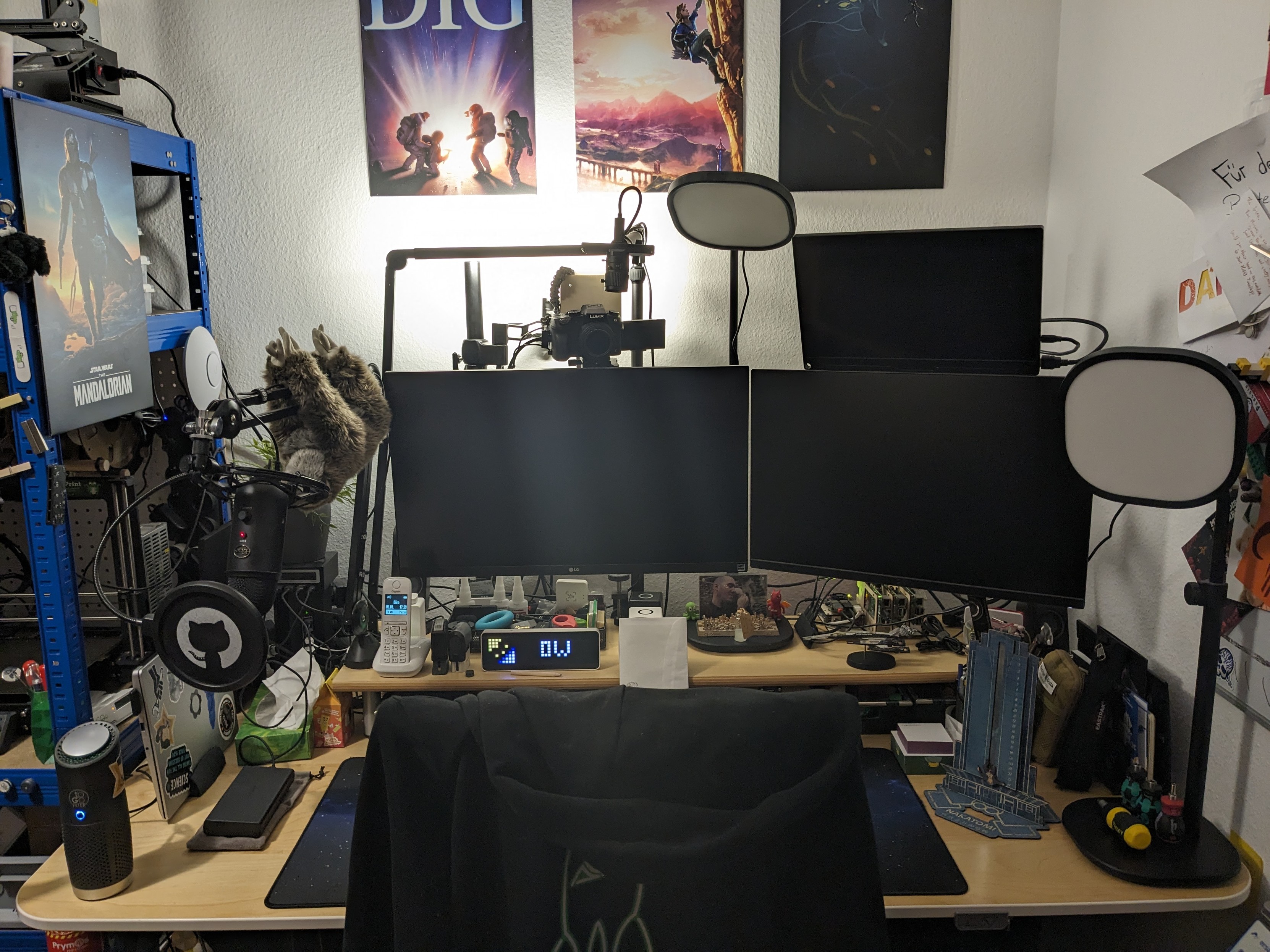 View towards the desk from being the chair. Three screens, Framework laptop vertical to the left, a bunch of steaming lights.