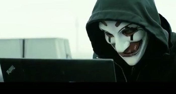 Screenshot from the movie “Who Am I” of a hacker in a scary clown mask at a laptop 