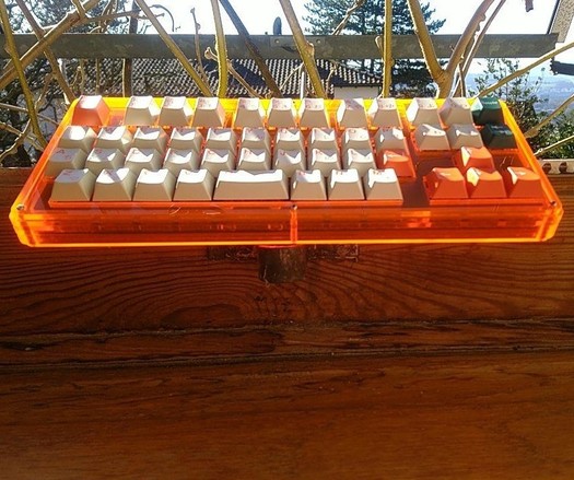 a custom Shambles keyboard from WorldspawnsKeebs in fluorescent orange acrylic with the orange on white, white on orange and white on dark green Nephlock GMK Kaiju keycap set.

It's sitting on a window sill and sun shines on it. Especially the bottom plate of the layered acrylic case glows from the incoming sunshine on the backside.