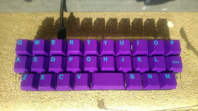 An Alpha keyboard, designed by PyrooL and sold by WorldspawnKeebs. As "Alpha" is a very ambiguous name, many call it Alpha28 as it only has 28 keys: 26 "alpha" keys (hence probably the original name), a 2u spacebar and a key left of the L key which can be used as layer switch key or Enter key, …

The keyboard has a half-ortholinear and half-staggered layout consisting of just three rows of keys. The two upper key rows have each 10 1u keys and are ortholinear to each other and contain the letter…