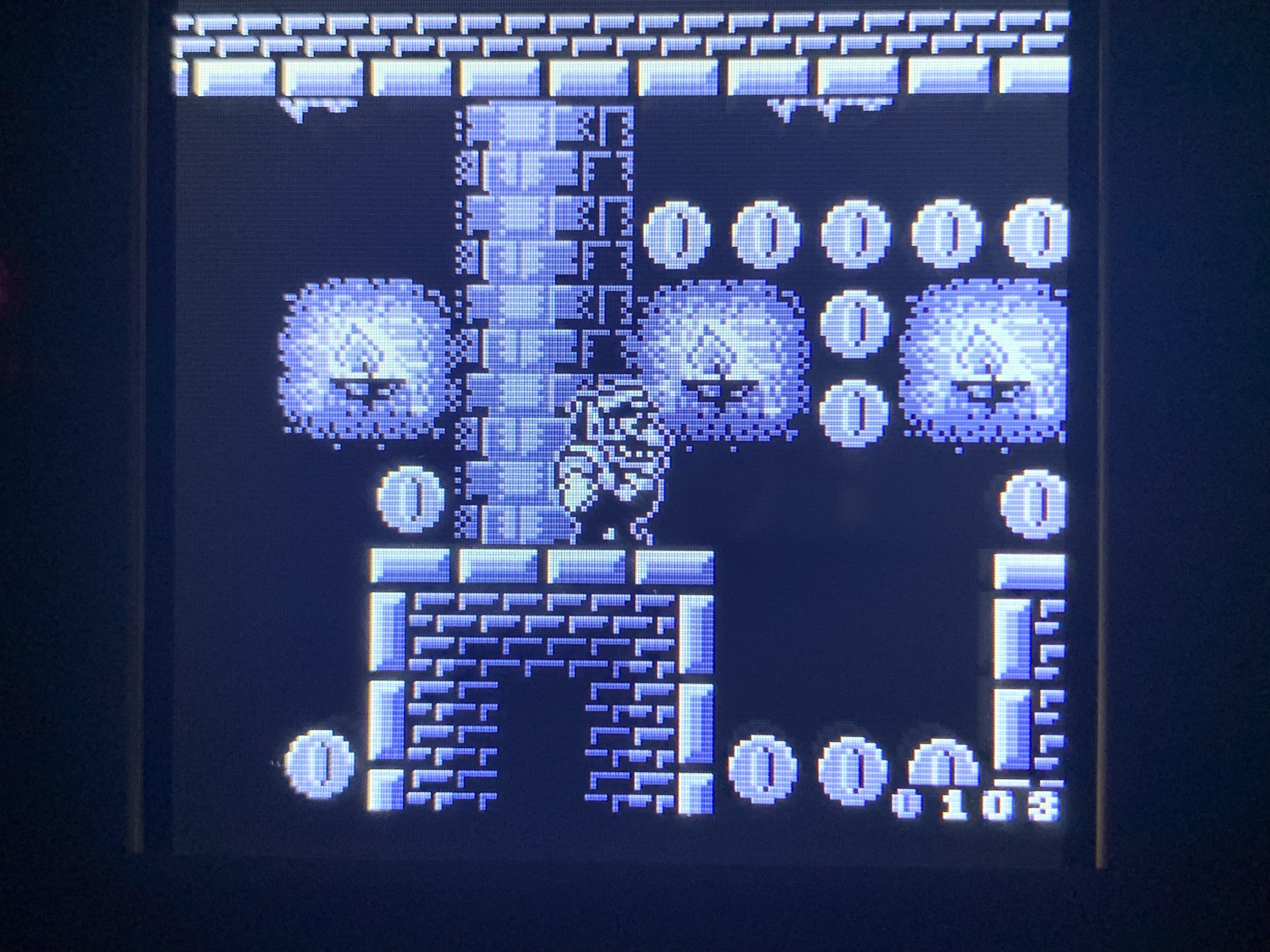Wario standing on a brick ledge in the scary mansion, candles in the background and many coins as well to collect. The image is monochromatic with several shades. 