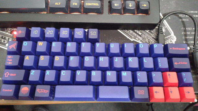 A 45% keyboard with four 12.75u rows and on top one 6u row slightly offset by three red LEDs on the left end.

It has cyan on a blue-ish purple alphas, red-ish pink on purple-ish dark blue modifiers and dark blue on red-ish pink arrow keys. The slash/question mark key is right of the curso up key.

There are several novelty keys used,.the left Alt key shows an icon of a DeLorean DMC12 timemachine from Back to the Future, the Windows key show a sunset icon, the tilde/backtick key a polygon unico…