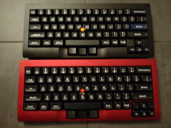 Two Tex Shura 60% keyboards with a 0.89u keycaps cursor cluster in the bottom right corner. They both have sculped, vintage looking white on black keycaps with legends in a typewriter font. They have a thumbstick between the G, H and B keys like ThinkPads and the black keys as mouse buttons in front of the spacebar, embedded in the at that position lowered frame.

Differences:

Top one has an officially black but actually more anthracite metal frame, bottom one a cold red frame.

Top one has an…