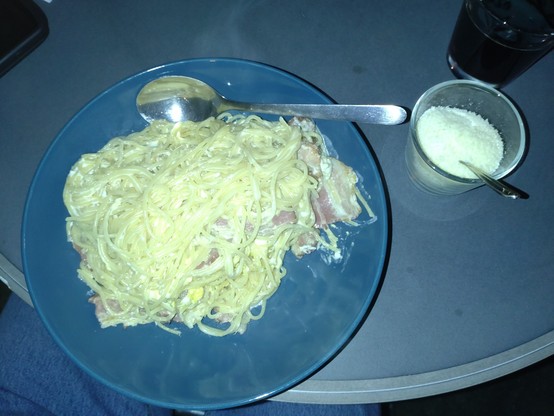 Spaghetti Carbonara with huge bacon stripes and glass of Parmesan hard cheese.