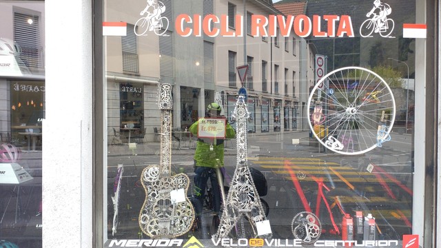 Shop window of a bicycle shop named "Cicli Rivolta" with two guitars made out of bicycle parts, mostly chainrings.