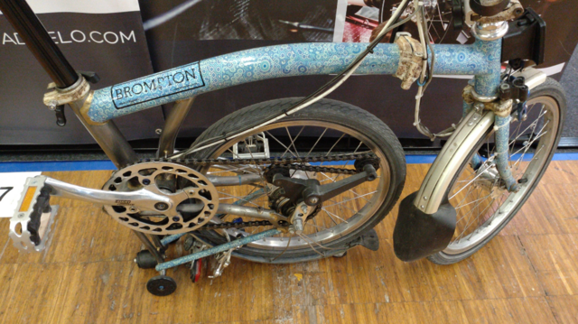 A hal folded Brompton with a blue on white flower pattern on most parts of the frame.