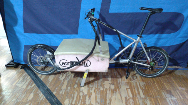 A cargobike which can be stored inside its own cargobox. It has written "verpacksti" on its box.