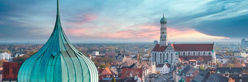 Ein Bild der Skyline von Augsburg im Sonnenuntergang. 
Oder ist es ein Morgengrauen, weil die Stadt jetzt digital voll durchstartet?