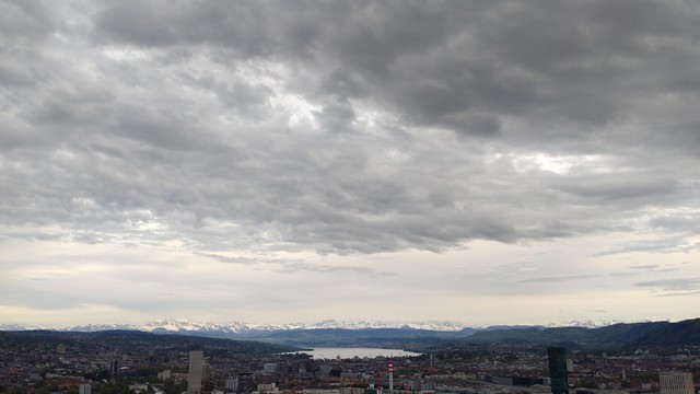 Panorama over Zurich with Lake Zurich and many snow covered mountains in the background. Grey clouds in the sky.