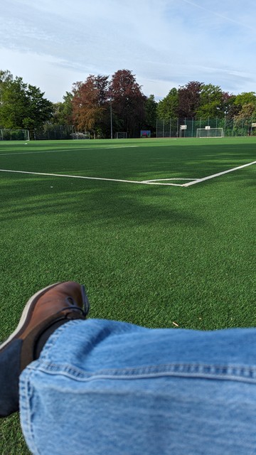 Foto leerer Fußballplatz, im Vordergrund unten blaue Jeans und mein rechter Schuh