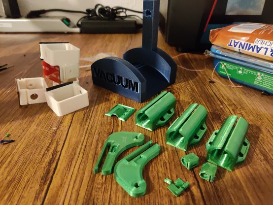 Photo of several printed plastic parts. A few green ones that are repair parts for another 3D printer, a blue vacuum hose wall holder and white cable management rings with double-sided tape attached to them.

There are some cables, cleaning equipment and the bottom of a resin printer in the background.