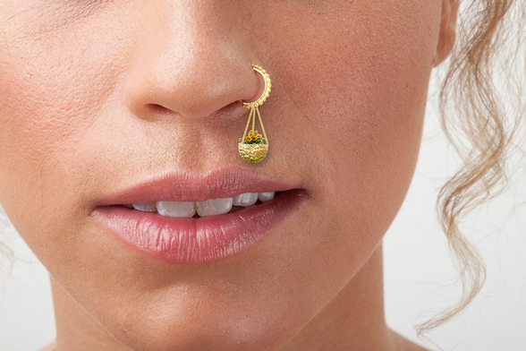 Eine junge Frau trägt einen goldenen Nasenring mit einer kleinen goldenen Blumenampel mit winzigen gelben Blümchen darin