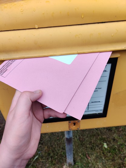 Eine Hand die zwei Briefwahlumschläge in einen Postkasten wirft