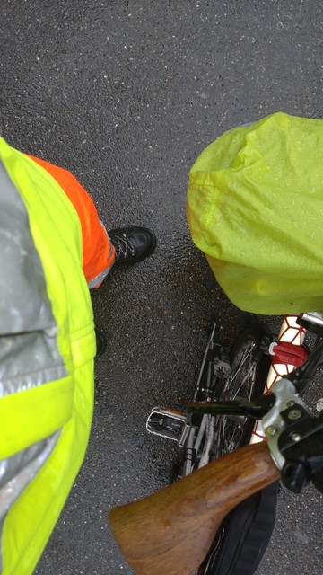 Looking down at my hi-viz safety and rain cloths (yellow jacket and orange pants) and the Brompton with front bag with a lime rain cover.
