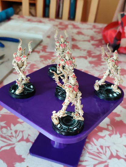 Five large bipedal robot miniatures, front view. They are wielding large guns, and have winged backpacks. Their primary colour is a bone white-brown, with dark pink detailing and gems. Their bases have black rims, white gems, and a dark green-black top surface with some glow and texture.