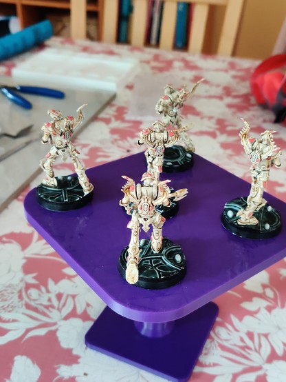 Five large bipedal robot miniatures, rear view. They are wielding large guns, and have winged backpacks. Their primary colour is a bone white-brown, with dark pink detailing and gems. Their bases have black rims, white gems, and a dark green-black top surface with some glow and texture.