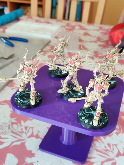 Five large bipedal robot miniatures, side view. They are wielding large guns, and have winged backpacks. Their primary colour is a bone white-brown, with dark pink detailing and gems. Their bases have black rims, white gems, and a dark green-black top surface with some glow and texture.
