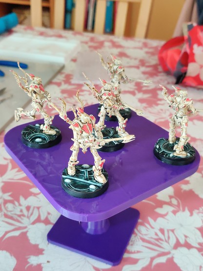 Five large bipedal robot miniatures, side view. They are wielding large guns, and have winged backpacks. Their primary colour is a bone white-brown, with dark pink detailing and gems. Their bases have black rims, white gems, and a dark green-black top surface with some glow and texture.