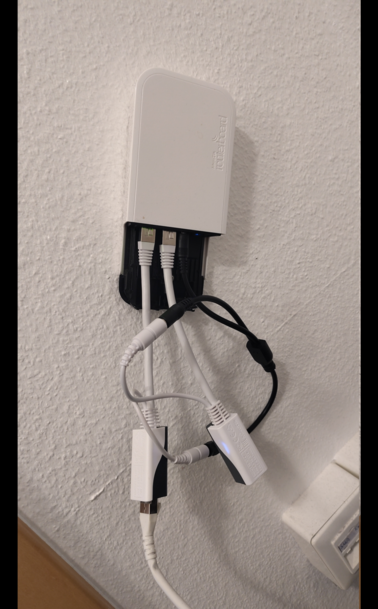 Ein Mikrotik Routerboard wAP AC mit zwei LAN-Ports hängt an einer Wand. Vor dem LAN1 hängt ein RBGPOE Power Injector, der POE aus dem ankommenden Kabel ausleitet. Der Strom wird über ein Y-Kabel in den wAP und einen weiteren RBPOE Power Injector gespeist, der am zweiten LAN-Port des WAP hängt.