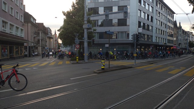 The bicycle demonstration rides around a sharp (60 degree) corner around a city building. Tramway tracks in the street they're coming from. View from the other side of the crossing. (Corker's view)