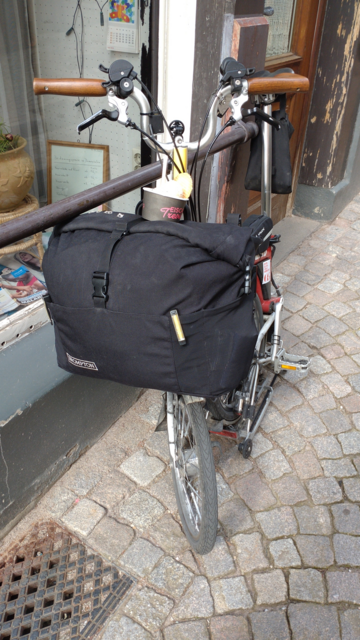 My red-white Brompton half-folded in front of a shop window in Laufenburg. There's a cup of ice cream standing on its black front bag.