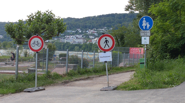 The pedestrian and bicycle path at the Rhine below Waldshut. You can see three traffic signs: A permanent white on blue sign saying "pedestrian way, bicyclists allowed" and two red-white temporary signs saying "pedestrians forbidden"bicycles forbidden". One of them has an a bit unprofessional black on white add-on sign saying "floodwater". (Nobody cared. 😊)