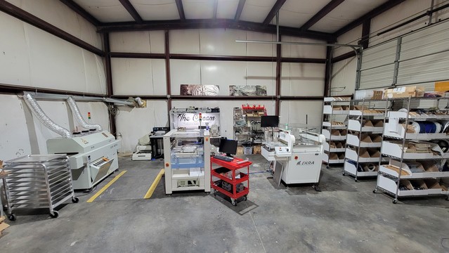 Picture of my home SMT line. From left to right: a rolling shelf of baker's racks, a reflow oven, a manncorp pnp, an ekra stencil printer, several rolling inventory shelves. 