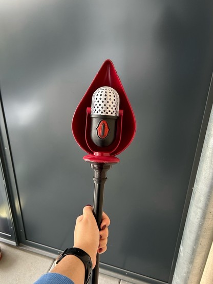 holding a staff with a red top and a silver perforated microphone inside.