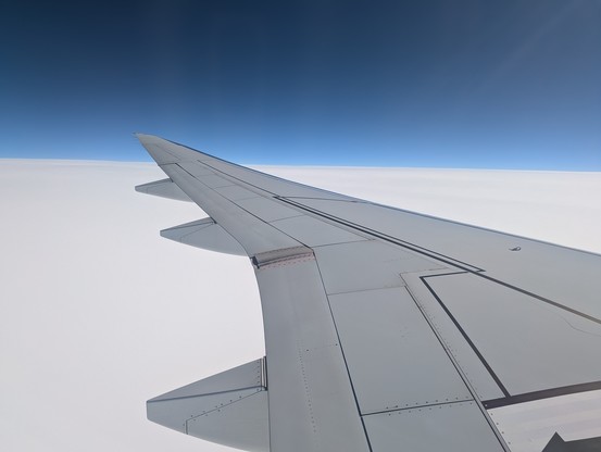 A photo of an aircraft wing, flying over a white blanket of cloud. Blue skies up above.