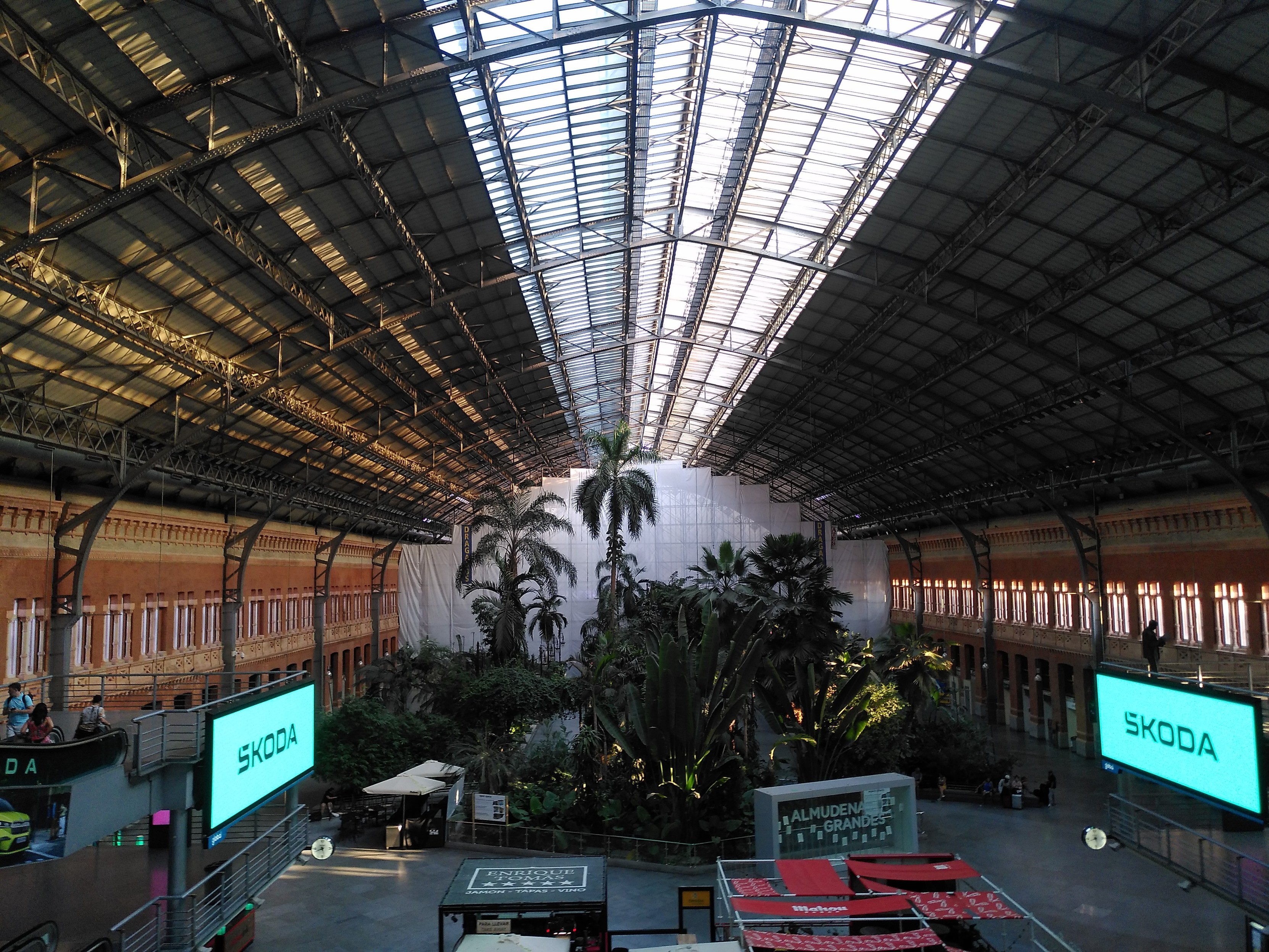 Alte Bahnhofshalle in Madrid Atocha. Backsteinwände und eine Stahlkonstruktion als Dach. Ähnlich wie die meisten europäischen Bahnhöfe aus dem 19 Jahrhundert. Nur sind da keine Gleise mehr sonder eine handvoll Palmen  füllen die leer anmutende Halle.