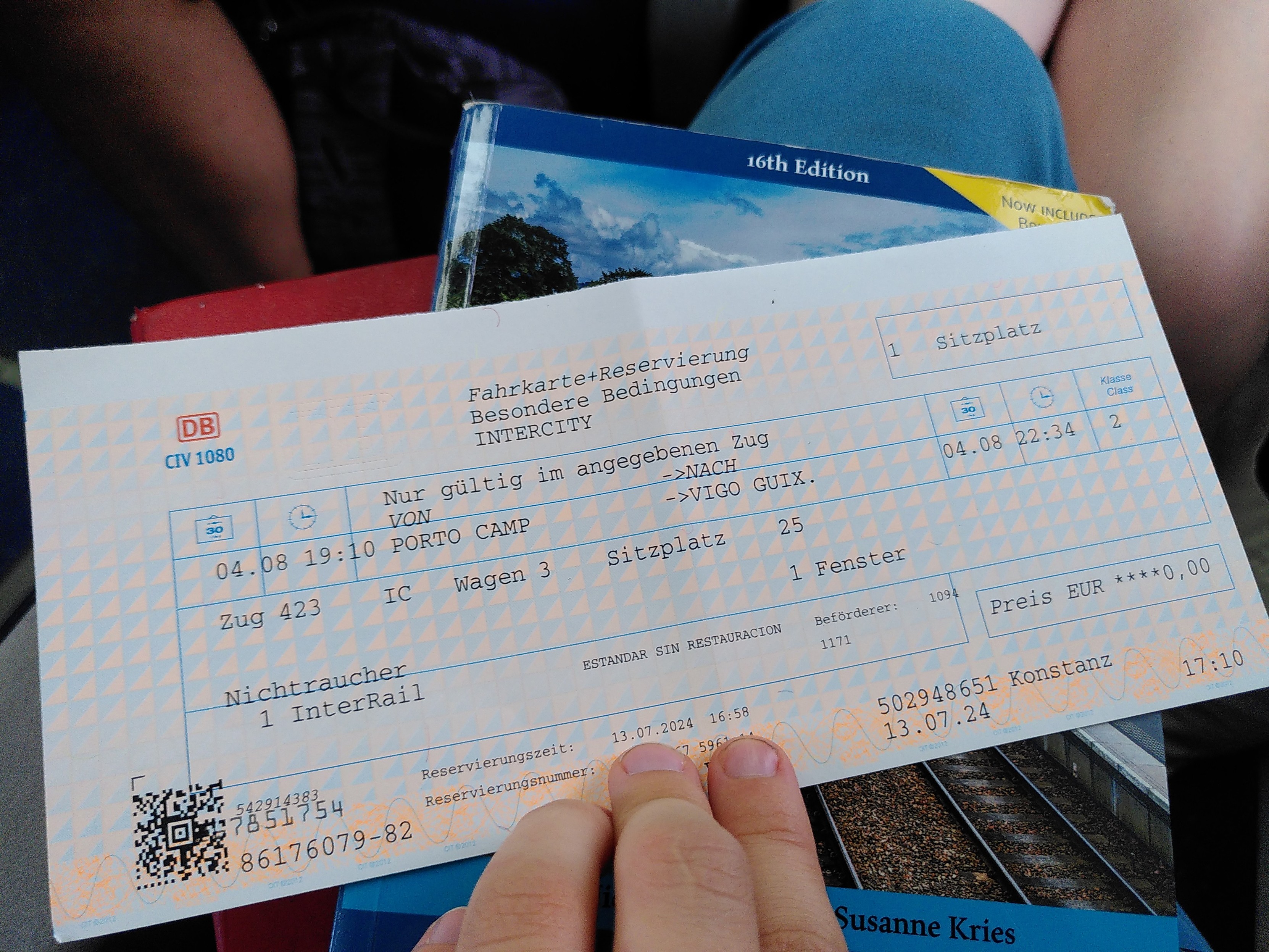 Altmodischer Papierfahrschein der Deutschen Bahn liegt auf meinem Schoß. Darunter das Buch Europe by Rail. Auf dem Fahrschein steht Reservierung von Porto nach Vigo. Preis 0€