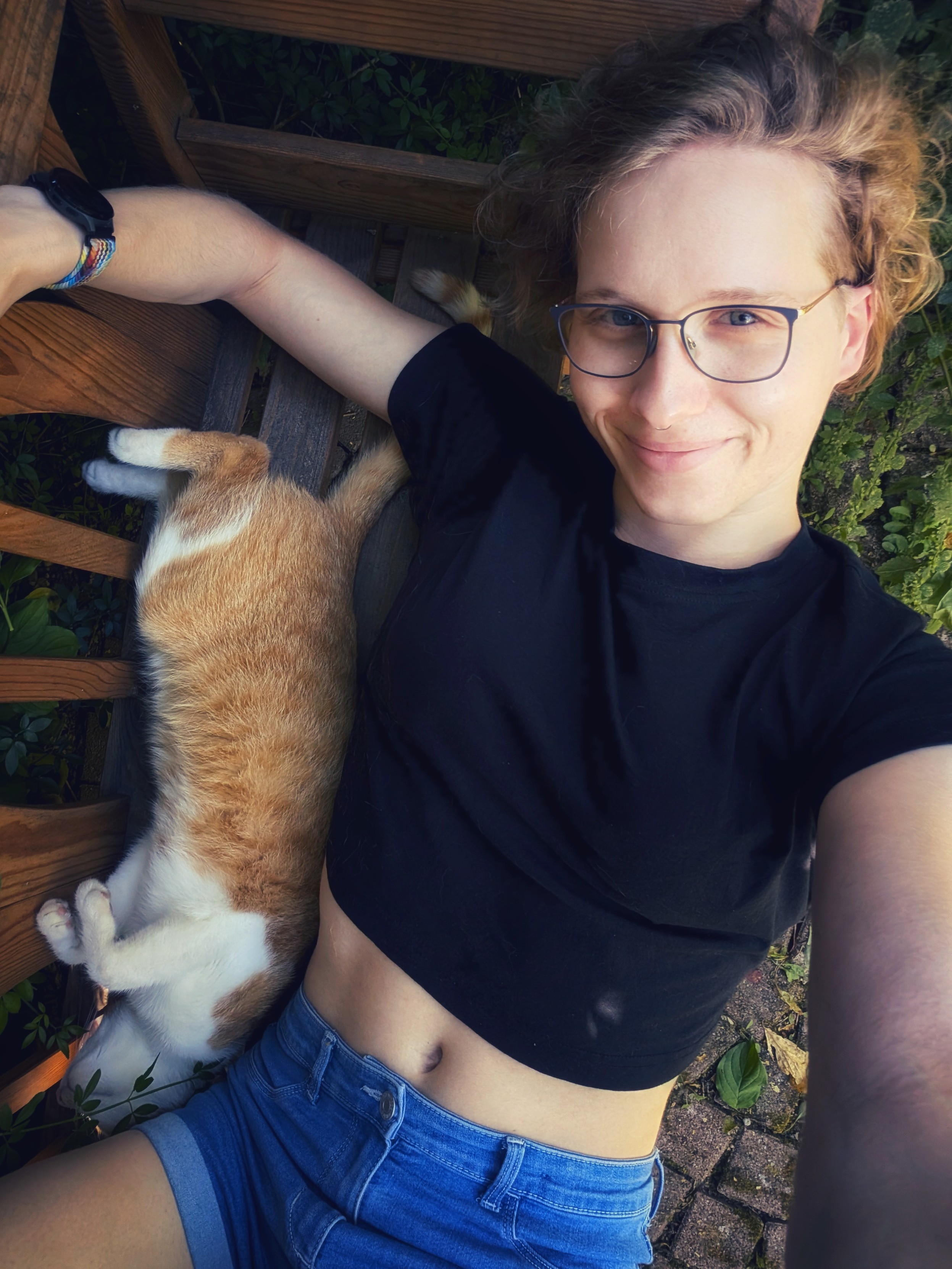 Selfie. Ich liege im Garten im Schatten auf einer Bank. Neben mir liegt eine rot weiße Katze 