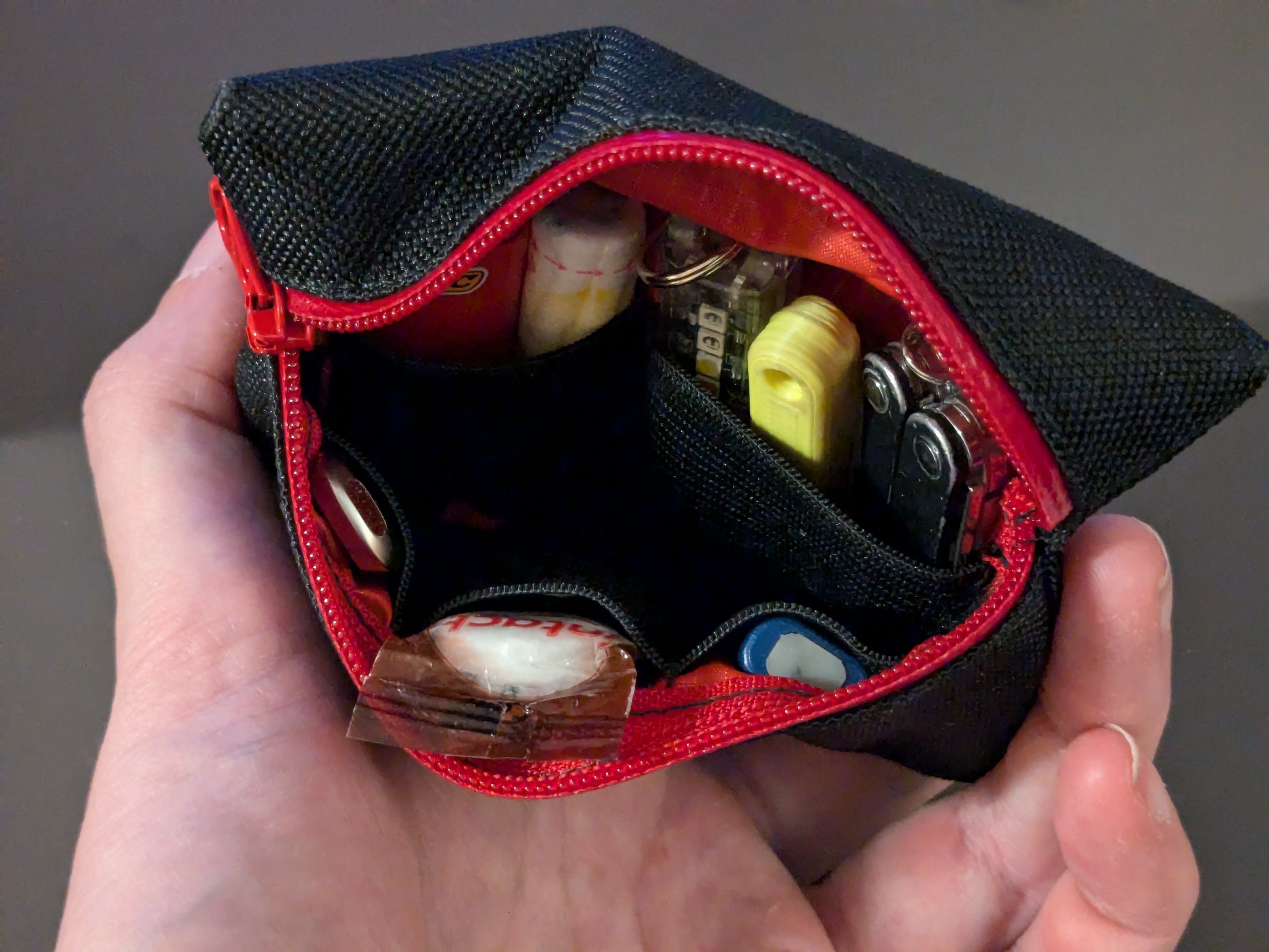 The pouch zipped and pushed open. The inside shows some small pockets created by black fabric stripes on top of the red inside.