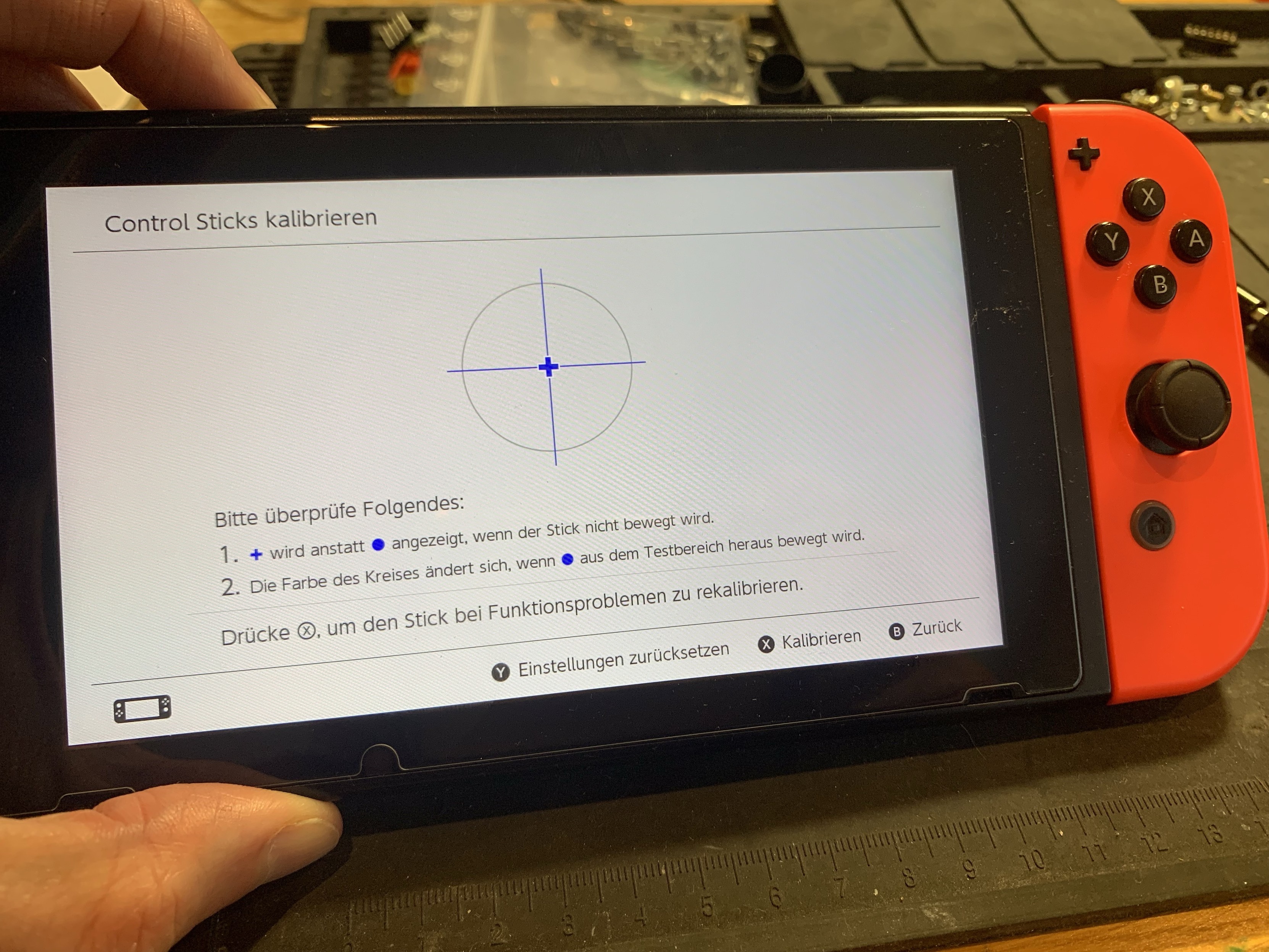 An image of a Nintendo Switch showing a screen for calibrating control sticks. The interface is in German, providing instructions for calibration with visual indicators. A hand is holding the console.