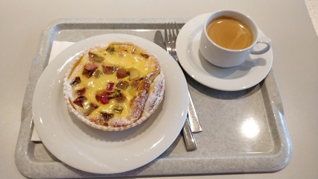 Kleines Tablett in der Kantiene mit einem Fruchtkuchen und einem Kaffee darauf.