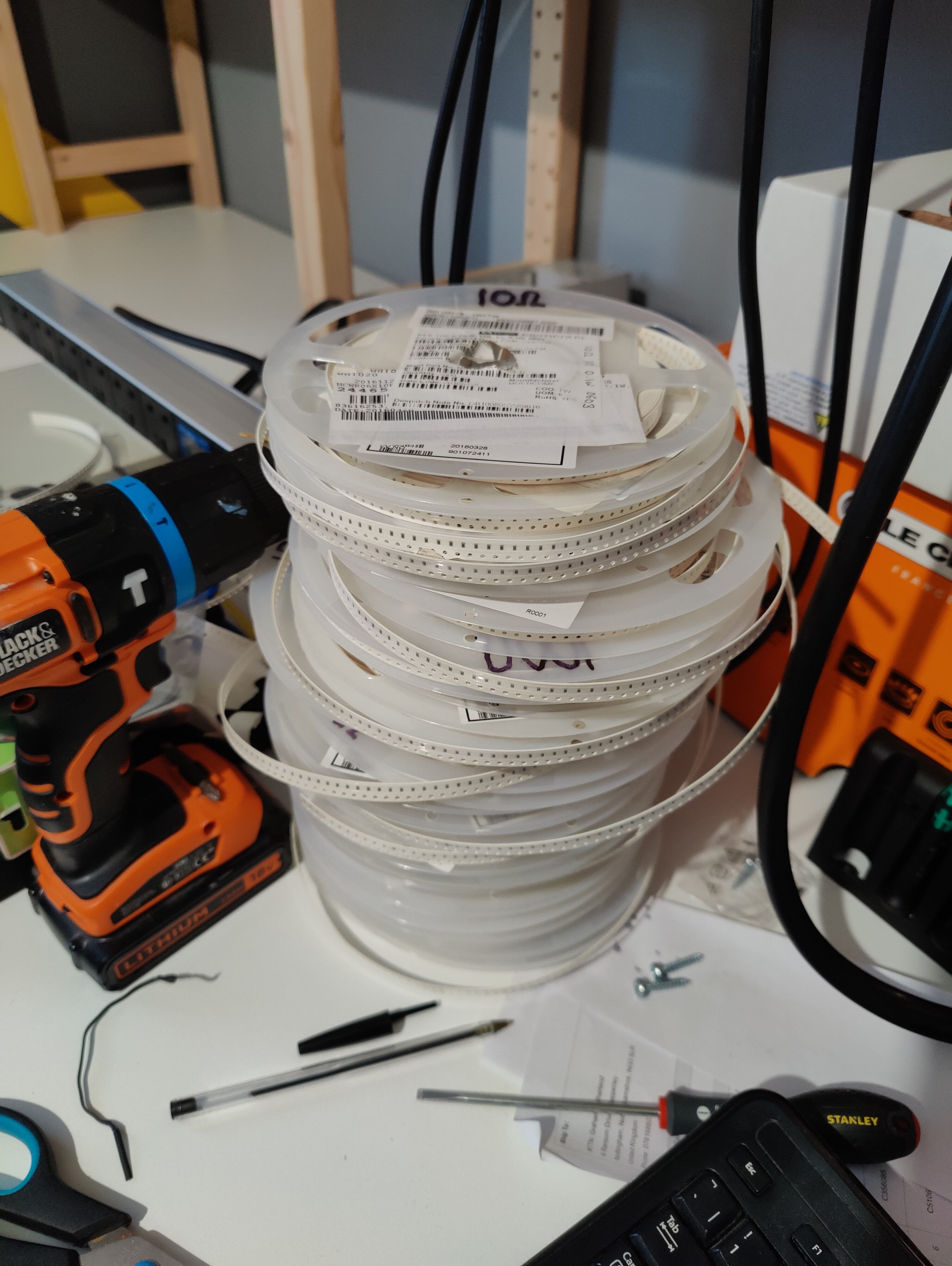 Stack of surface mount reels containing resistors and capacitors, on a somewhat messy desk.