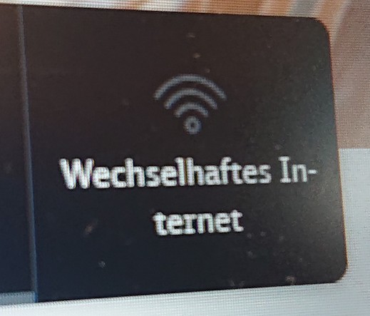 Foto eines Displays, vergrößert, Ausschnitt,
WLAN Symbol in grauf auf dunkelgrau Grund, darunter in weißer Schrift "Wechselhaftes Internet". 