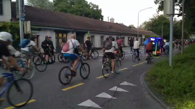 Video von nahezu der gesamten Critical Mass mit Blick in Fahrtrichtung aus einer Strasseneinbiegung heraus. Es sind viele hundert Velos und Personen unterschiedlichster Couleur zu sehen.