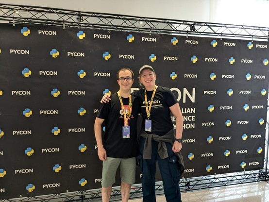 Me and Jacopo are posing in front of the photo wall at PyCon. We are both smiling.