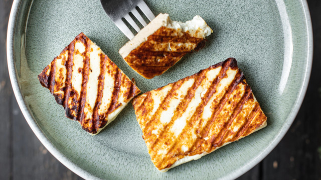 Teller mit drei Stück gegrilltem Halloumi-Käse, ein Stück auf einer Gabel, bereits angebissen