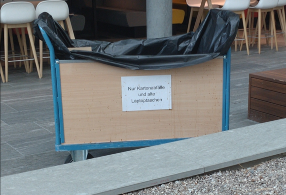 Abfallwägelchen mit Schild "Nur Kartonabfälle und alte Laptoptaschen"