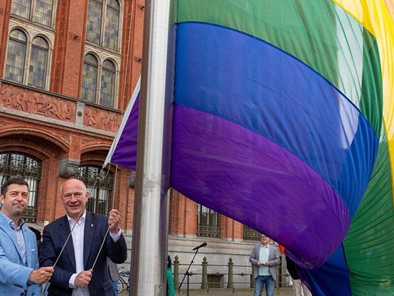 Wegner und noch jemand hissen die Regenbogenflagge vor dem Berliner Rathaus